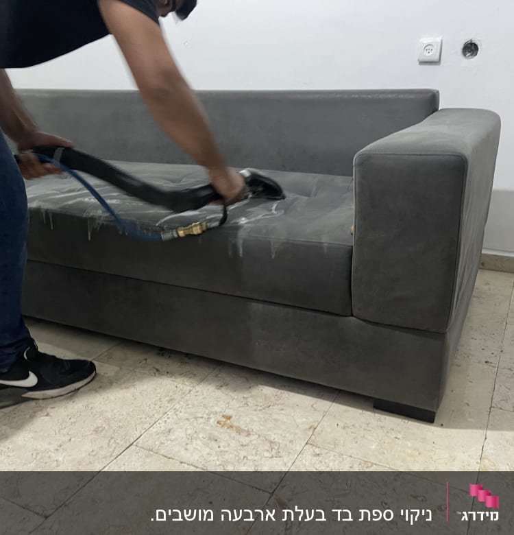 אדם מנקה ספה אפורה עם מכשיר ניקוי